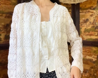 May include: White crochet cardigan with a delicate lace pattern. The cardigan has long sleeves and a v-neck.