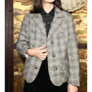 May include: A gray and black plaid blazer with a button closure. The blazer has two pockets on the front and a single button on each cuff.