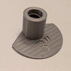 May include: A gray 3D-printed object with a cylindrical top and a semi-circular base. The base has a ribbed texture and the number "311" is printed on it. The cylindrical top has a threaded interior.
