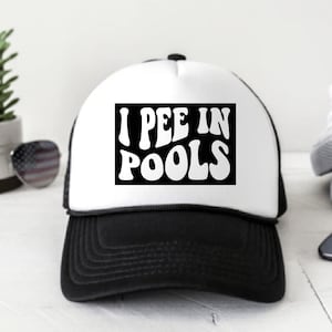 Puede incluir: Una gorra de camionero blanca y negra con una malla negra en la parte posterior. La parte delantera de la gorra tiene un gráfico blanco que dice "I PEE IN POOLS" en una fuente retro.