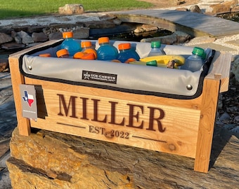 May include: A wooden cooler with a grey liner, filled with drinks and fruit. The cooler is personalised with the name "MILLER" and the text "EST. 2022".