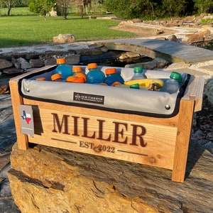 Cedar Wood ice chest with Removable insulated liner inside, Sitting on a rock with a personalization engraved across the front of the cooler
