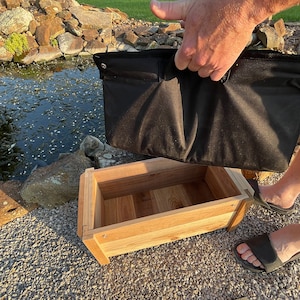 May include: A wooden planter box with a black fabric liner. The liner is being lifted out of the box by a hand.