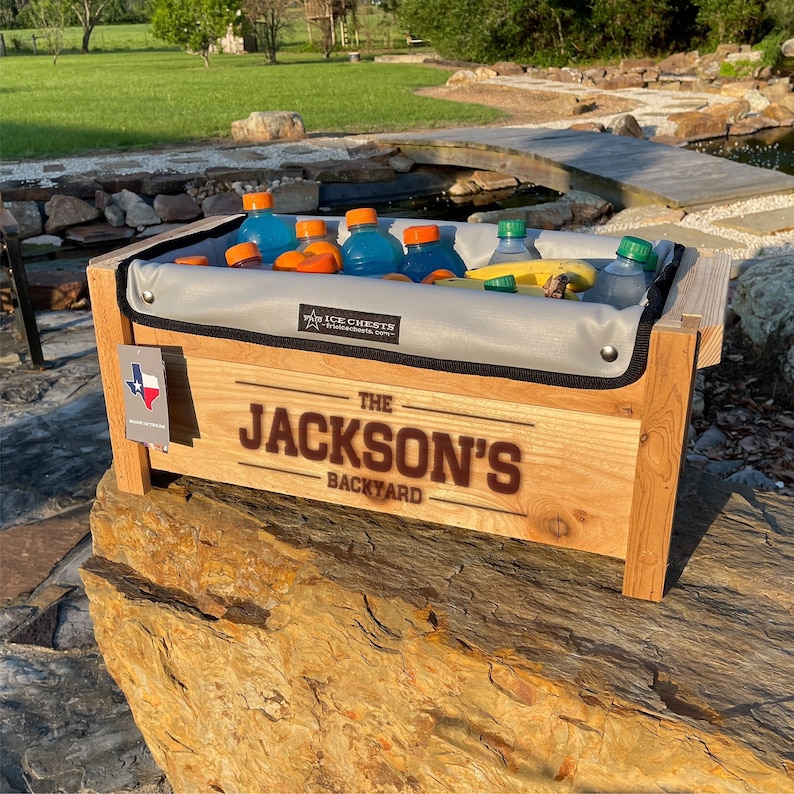 Cedar Wood ice chest with Removable insulated liner inside, Sitting on a rock with a personalization engraved across the front of the cooler