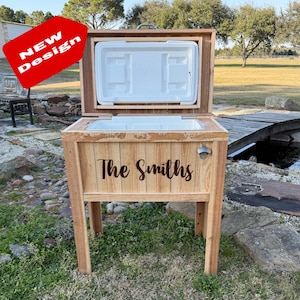 以下が含まれることがあります： 「The Smiths」と刻まれた木製のクーラーボックス。クーラーボックスには栓抜きが内蔵されており、木製のスタンドの上に置かれています。クーラーボックスは開いており、蓋は持ち上げられています。