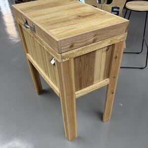 Pode incluir: Uma caixa de gelo de madeira com uma tampa articulada e al&ccedil;as de metal. A caixa de gelo &eacute; feita de madeira natural com um acabamento marrom claro. Tem um visual r&uacute;stico e &eacute; perfeita para entretenimento ao ar livre.