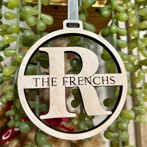 May include: A wooden Christmas ornament with a cutout of the letter "R" and the text "THE FRENCHS" on a white ribbon.