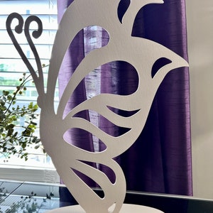 May include: White wooden butterfly sculpture with intricate cutouts. The butterfly is standing on a round base.