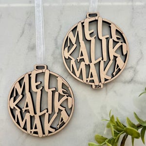 May include: Two wooden Christmas ornaments with the words "Merry Christmas" written in a stylized font. The ornaments are hanging from white ribbon.