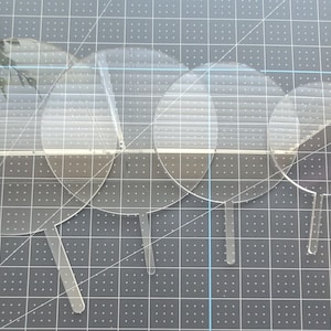 May include: Five clear acrylic cake circles with handles, arranged in descending size order. The circles are on a gray grid surface.
