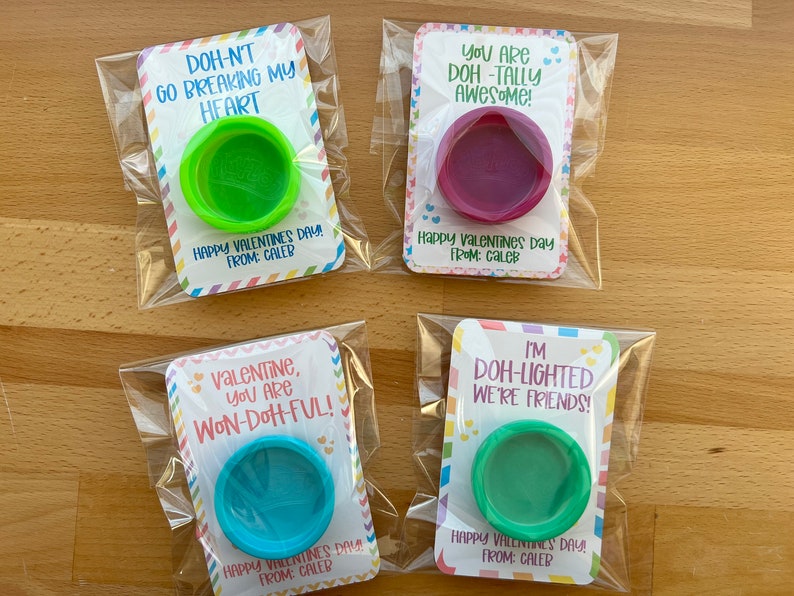 May include: Four Valentine's Day cards with colorful playdough containers. Each card has a different pun: "Doh-nt go breaking my heart," "You are Doh-tally Awesome!", "Valentine, you are Won-Doh-ful!", and "I'm Doh-lighted we're friends!" Each card is from Caleb.