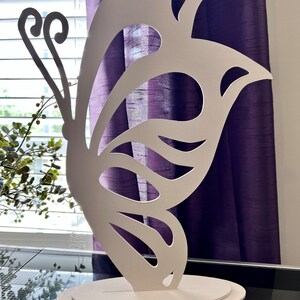 May include: White butterfly-shaped cutout on a white base. The butterfly has intricate cutouts and a delicate design.