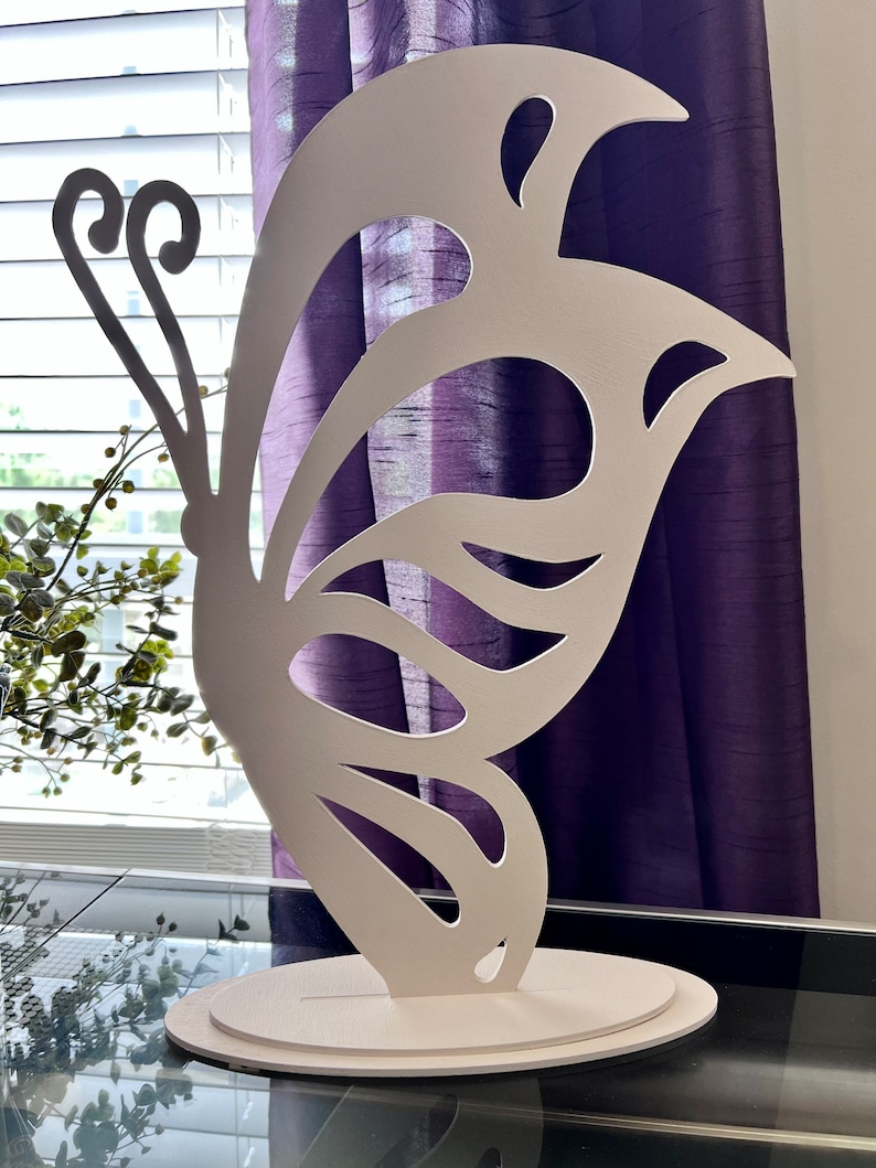 May include: White butterfly-shaped cutout on a white base. The butterfly has intricate cutouts and a delicate design.