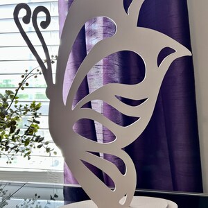 May include: White wooden butterfly cutout with a decorative base. The butterfly has a detailed design with cutouts in the wings. The base is a simple oval shape.