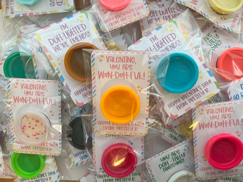 May include: A collection of Valentine's Day gifts featuring small containers of colorful playdough. Each container is packaged with a card that reads "Valentine, you are Won-Doh-Ful!" or "I'm Doh-lighted we're friends!"