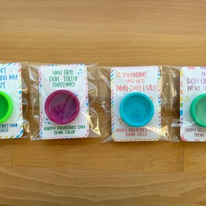 May include: Four Valentine's Day gifts in clear plastic packaging. Each card has a different message and a small container of colorful playdough. The messages include puns like "Doh-n't go breaking my heart."