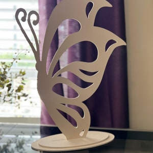 May include: White butterfly-shaped decorative stand with a cutout design. The stand is made of a lightweight material and has a circular base.