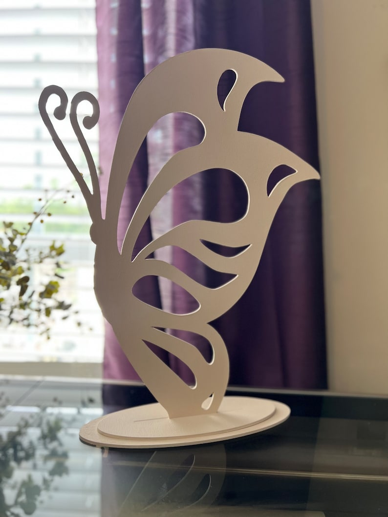 May include: White butterfly-shaped decorative stand with a cutout design. The stand is made of a lightweight material and has a circular base.