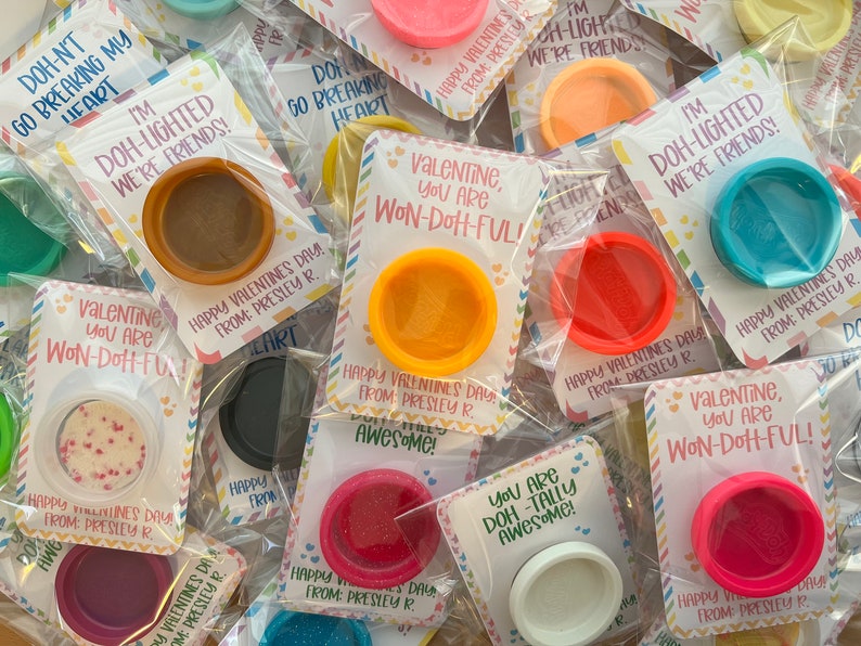 May include: Valentine's Day gifts featuring small, colorful containers of playdough. Each container is packaged with a card that has a Valentine's Day message. The colors of the playdough include pink, orange, blue, and white.