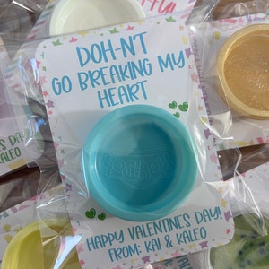 May include: Valentine's Day gifts featuring small containers of colorful Play-Doh. Each container is packaged with a card that reads "Doh-nt Go Breaking My Heart" and "Happy Valentine's Day! From: Kai & Kaleo."