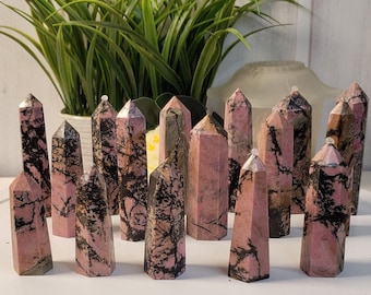 Puede incluir: Una colección de puntas de piedras preciosas pulidas de color rosa y negro. Las puntas están dispuestas en semicírculo sobre una superficie blanca.