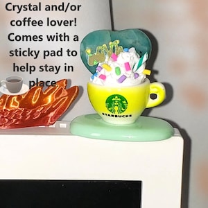 May include: A yellow Starbucks coffee cup figurine with whipped cream, sprinkles, and a heart-shaped topper. The figurine sits on a green base. Text on the image reads "Desk Gift and Decor Perfect for your Crystal and/or coffee lover!"