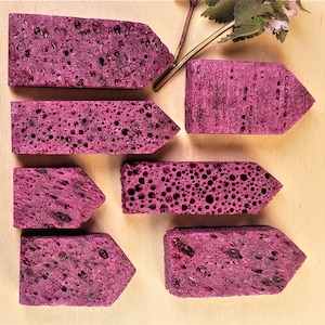 May include: Seven purple, arrow-shaped, porous, sponge-like objects on a light brown wooden surface.