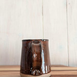 Puede incluir: Una taza de cer&aacute;mica marr&oacute;n con cuerpo redondeado y un asa ancha. La taza tiene un acabado brillante y una base ligeramente texturizada.