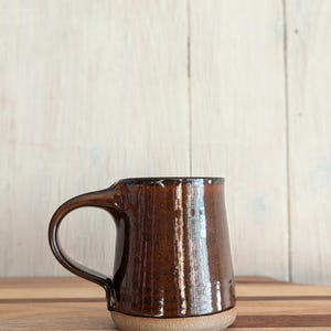 Puede incluir: Una taza de cer&aacute;mica marr&oacute;n con una base ancha y un asa redondeada. La taza tiene un acabado brillante y un esmalte moteado.