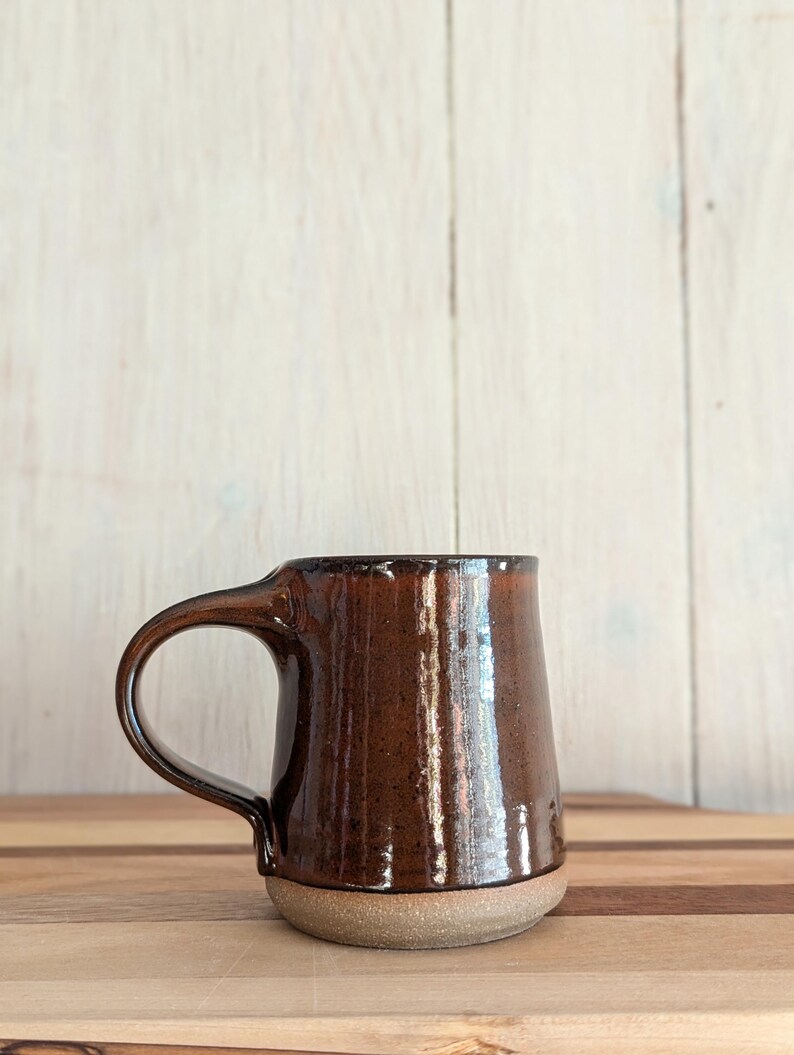 Puede incluir: Una taza de cer&aacute;mica marr&oacute;n con una base ancha y un asa redondeada. La taza tiene un acabado brillante y un esmalte moteado.