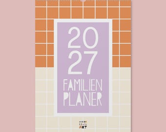 May include: A wall calendar for the year 2027 with a spiral binding at the top. The design features a grid pattern with orange squares on the top half and cream squares on the bottom. A central lavender rectangle displays the text 2027 FAMILIEN PLANER.