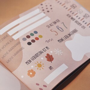 May include: A pink and white baby book with a section for personal information, including name, nickname, birthday, and favorite things. The book features a variety of illustrations, including a star, a snowflake, a sun, and a leaf.