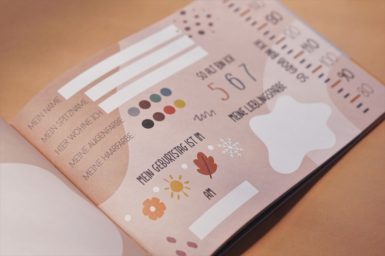 May include: A pink and white baby book with a section for personal information, including name, nickname, birthday, and favorite things. The book features a variety of illustrations, including a star, a snowflake, a sun, and a leaf.