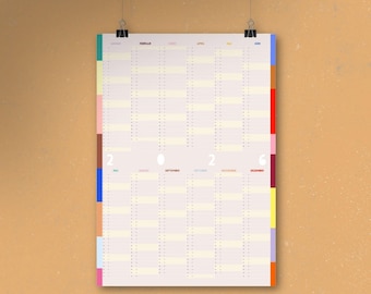 Könnte beinhalten: Ein Jahreskalender mit cremefarbenem Hintergrund, der an schwarzen Clips hängt. Der Kalender hat Spalten für jeden Monat und Zeilen für jeden Tag. Die linken und rechten Ränder haben farbige vertikale Streifen. Das Jahr "2026" ist in der Mitte aufgedruckt.