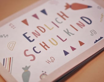 May include: A pink card with the text "ENDLICH SCHULKIND" in colorful letters. The card is decorated with colorful geometric shapes, including triangles, a protractor, and a musical note.