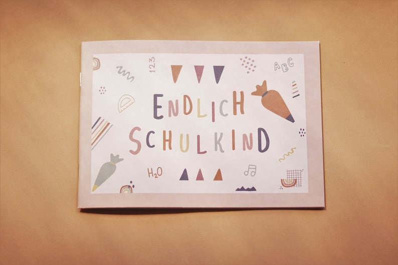 May include: A pink card with the text "ENDLICH SCHULKIND" in colorful letters. The card is decorated with various colorful illustrations, including a rainbow, a carrot, a music note, and a protractor.