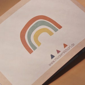 May include: A white card with a rainbow design in shades of red, orange, yellow, green, and blue. Three small triangles in blue, red, and purple are below the rainbow. The text "www.modernkidsart.de" is printed below the triangles.