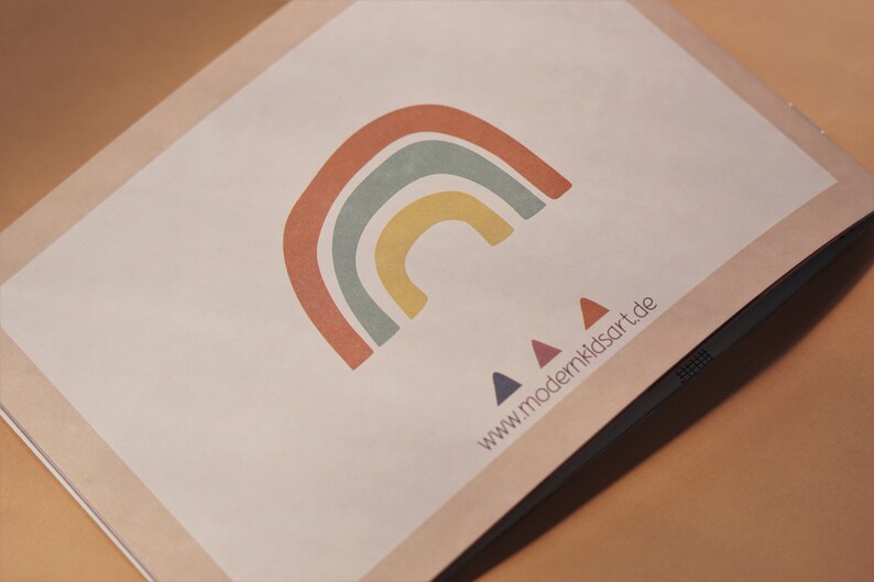 May include: A white card with a rainbow design in shades of red, orange, yellow, green, and blue. Three small triangles in blue, red, and purple are below the rainbow. The text "www.modernkidsart.de" is printed below the triangles.