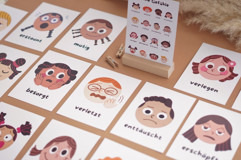 May include: A set of flashcards featuring illustrated faces with different emotions, each card has a German word describing the emotion. The words include "erstaunt", "mutig", "besorgt", "verletzt", "entt&auml;uscht", "ersch&ouml;pft", "verlegen".