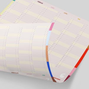May include: A rolled-up, cream-colored calendar with vertical columns and horizontal rows. The calendar has colorful side tabs in shades of pink, blue, brown, and red. Months are printed in various colors along the top and side edges.