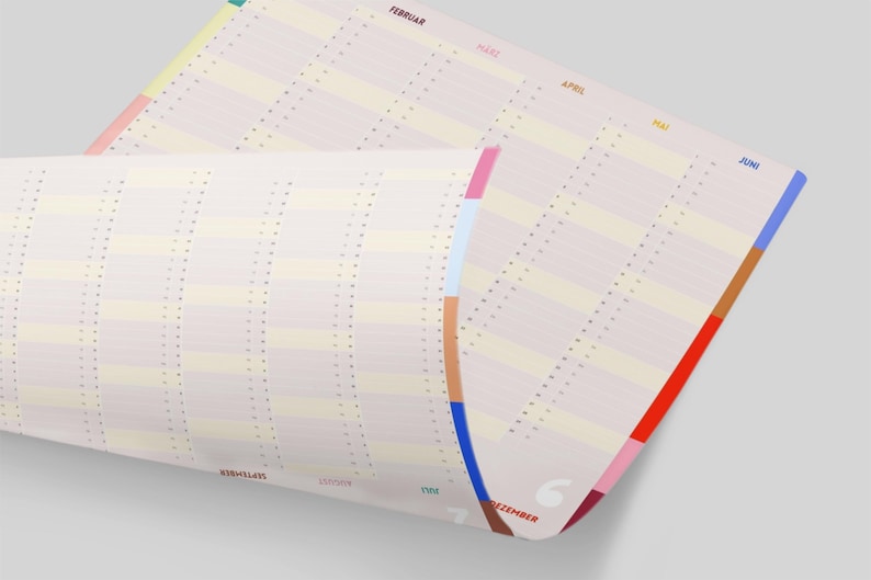 May include: A rolled-up, cream-colored calendar with vertical columns and horizontal rows. The calendar has colorful side tabs in shades of pink, blue, brown, and red. Months are printed in various colors along the top and side edges.