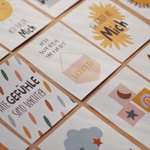 May include: A set of colorful affirmation cards with illustrations and text in German. The cards feature phrases like "Ich liebe mich" (I love myself), "Alle Gef&uuml;hle sind wichtig" (All feelings are important), and "Ich werde geliebt" (I am loved).