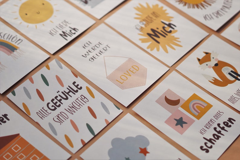 May include: A set of colorful affirmation cards with illustrations and text in German. The cards feature phrases like "Ich liebe mich" (I love myself), "Alle Gef&uuml;hle sind wichtig" (All feelings are important), and "Ich werde geliebt" (I am loved).