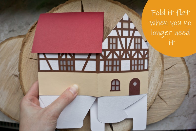 May include: A papercraft house with a red roof, white walls, and brown trim. The house is folded flat and has a text label that says "Fold it flat when you no longer need it".