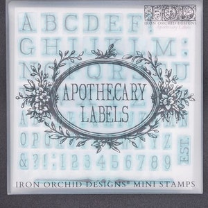 May include: Clear plastic package containing a set of apothecary label stamps. The stamps include letters, numbers, and punctuation. The words "APOTHECARY LABELS" are in a decorative oval frame. The package also includes the text "IRON ORCHID DESIGNS MINI STAMPS".
