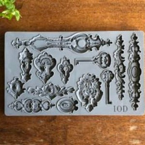 May include: A gray silicone mold featuring various antique key and lock designs. The mold includes ornate keys, keyholes, and decorative embellishments. The letters "IOD" are visible on the bottom right corner of the mold.
