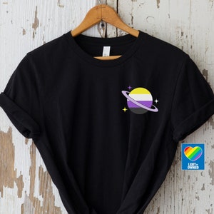 May include: Black t-shirt featuring a yellow, purple and black planet graphic with a ring and stars. The text "LGBT+ OWNED" is on a blue heart sticker.