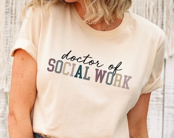 May include: A soft cream colored t-shirt with the text "doctor of SOCIAL WORK" in black and colorful letters.