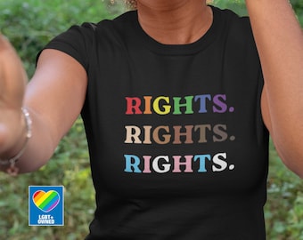 May include: A black t-shirt with the word "RIGHTS." repeated three times in rainbow colours. The shirt is being worn by a person with dark skin and curly hair. A small rainbow heart with the text "LGBT+ OWNED" is in the bottom left corner of the image.