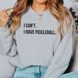 K&ouml;nnte beinhalten: Ein graues Sweatshirt mit dem Text "I can't. I have pickleball." auf der Vorderseite.